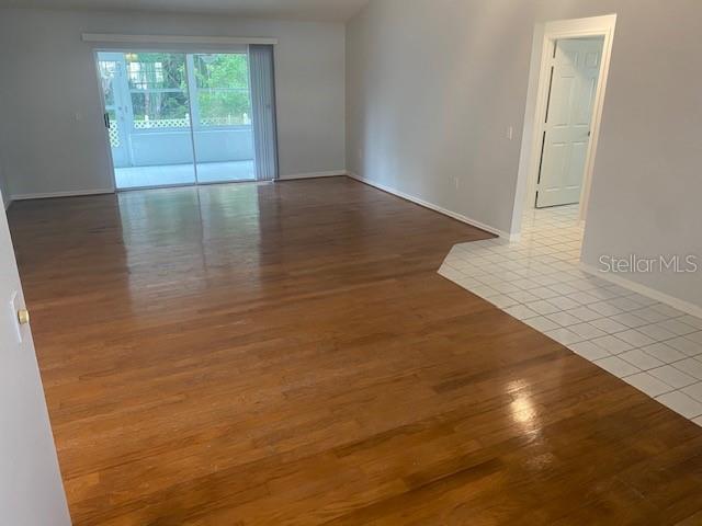 An empty room features hardwood flooring, a sliding glass door, and a tiled entryway — 7050 WOODIBIS DRIVE, NEW PORT RICHEY, FL