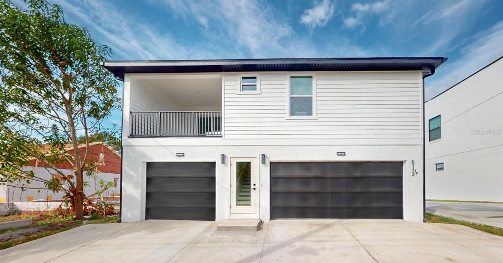 A two-story house with white siding, two dark garage doors, and an upper-level balcony — 5112 3RD AVENUE N, ST PETERSBURG, FL