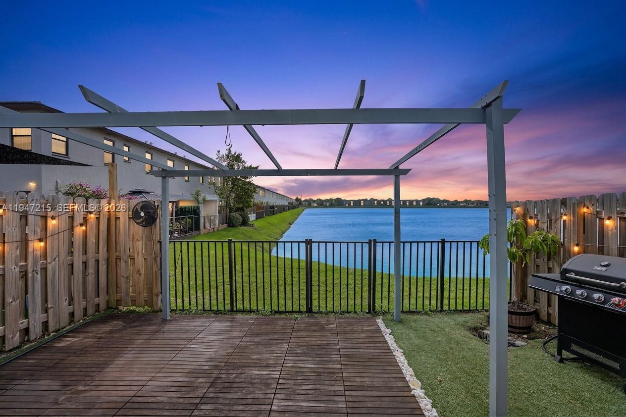 A wooden deck with a pergola overlooks a lake behind a fenced backyard — 544 NE 206th Ln, Miami FL 33179, MIAMI, FL
