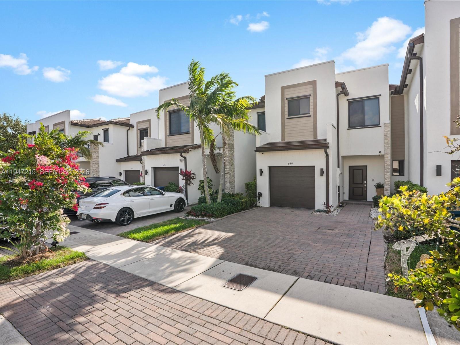 A row of modern two-story townhouses with attached garages and paved driveways under a blue sky — 544 NE 206th Ln, Miami FL 33179, MIAMI, FL