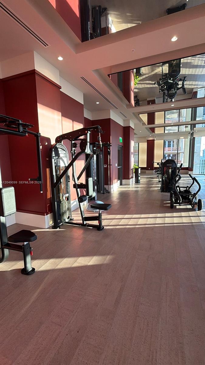 A gym features red walls, light wood flooring, and various strength training machines — 11 NE 6th St # 515, Miami FL 33132, MIAMI, FL
