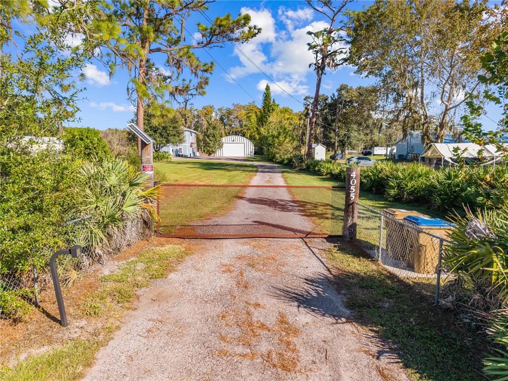 A gravel driveway leads to a gated entrance with a metal building in the background — 4055 EDSEL AVENUE, ST CLOUD, FL