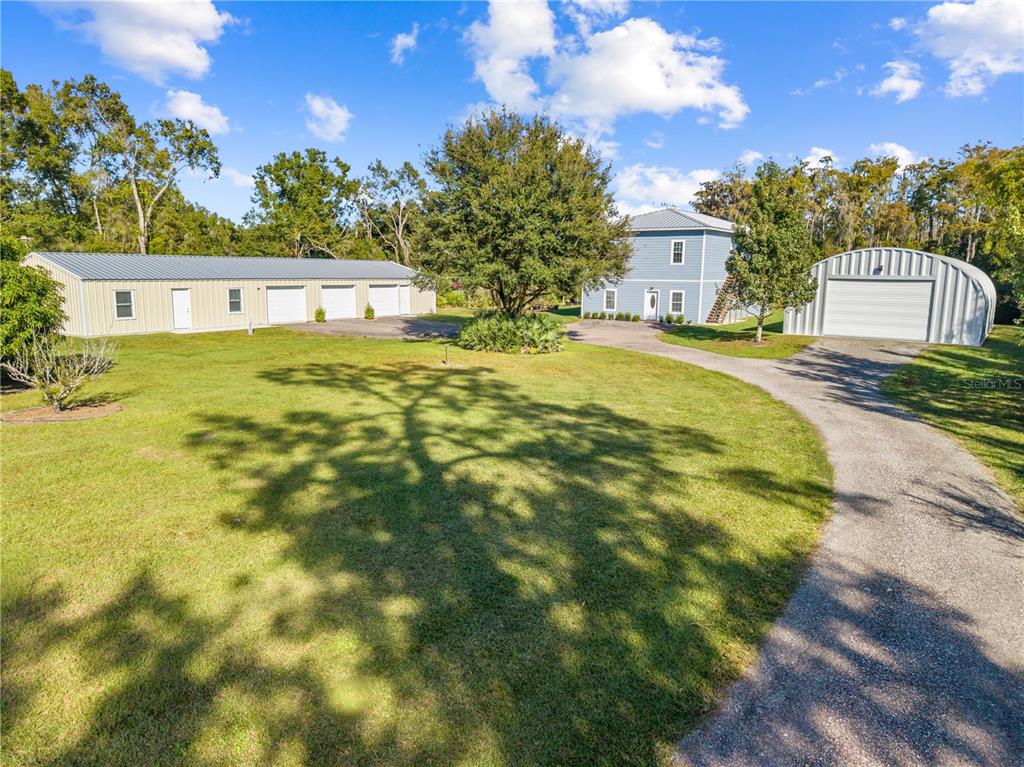 A blue two-story house sits on a grassy lot with two large metal outbuildings — 4055 EDSEL AVENUE, ST CLOUD, FL