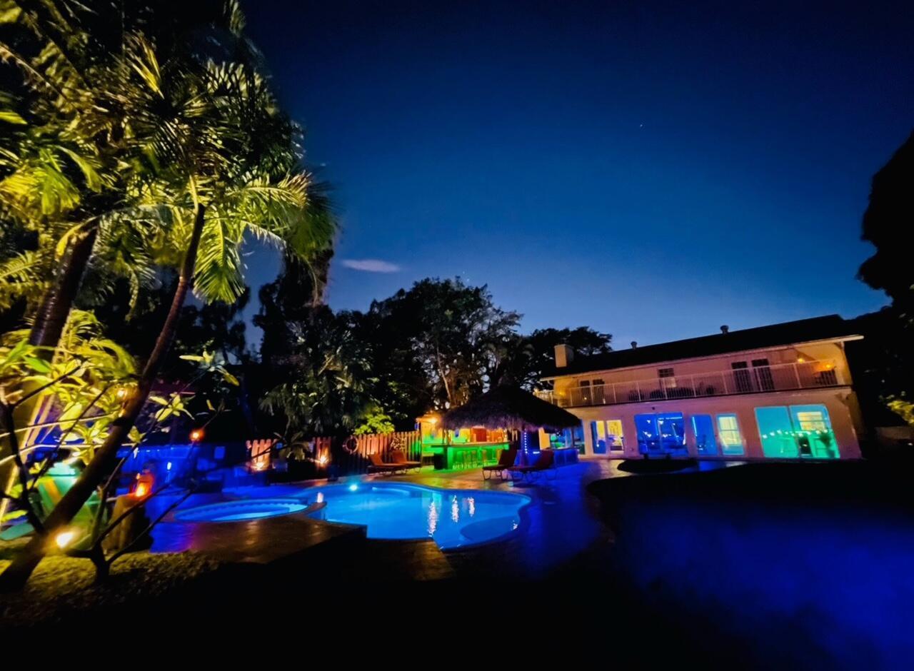 A backyard swimming pool and tiki bar are illuminated at night beside a two-story house — 6850 Eastview Drive, Lake Worth FL 33462, LAKE WORTH, FL