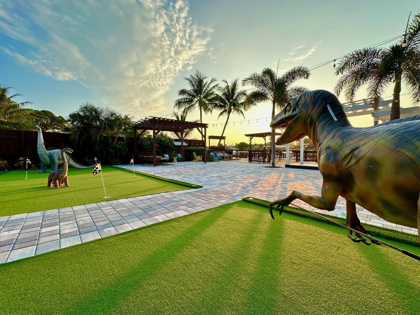 A backyard putting green features dinosaur statues, a paved patio, and a wooden pergola at sunset — 6850 Eastview Drive, Lake Worth FL 33462, LAKE WORTH, FL