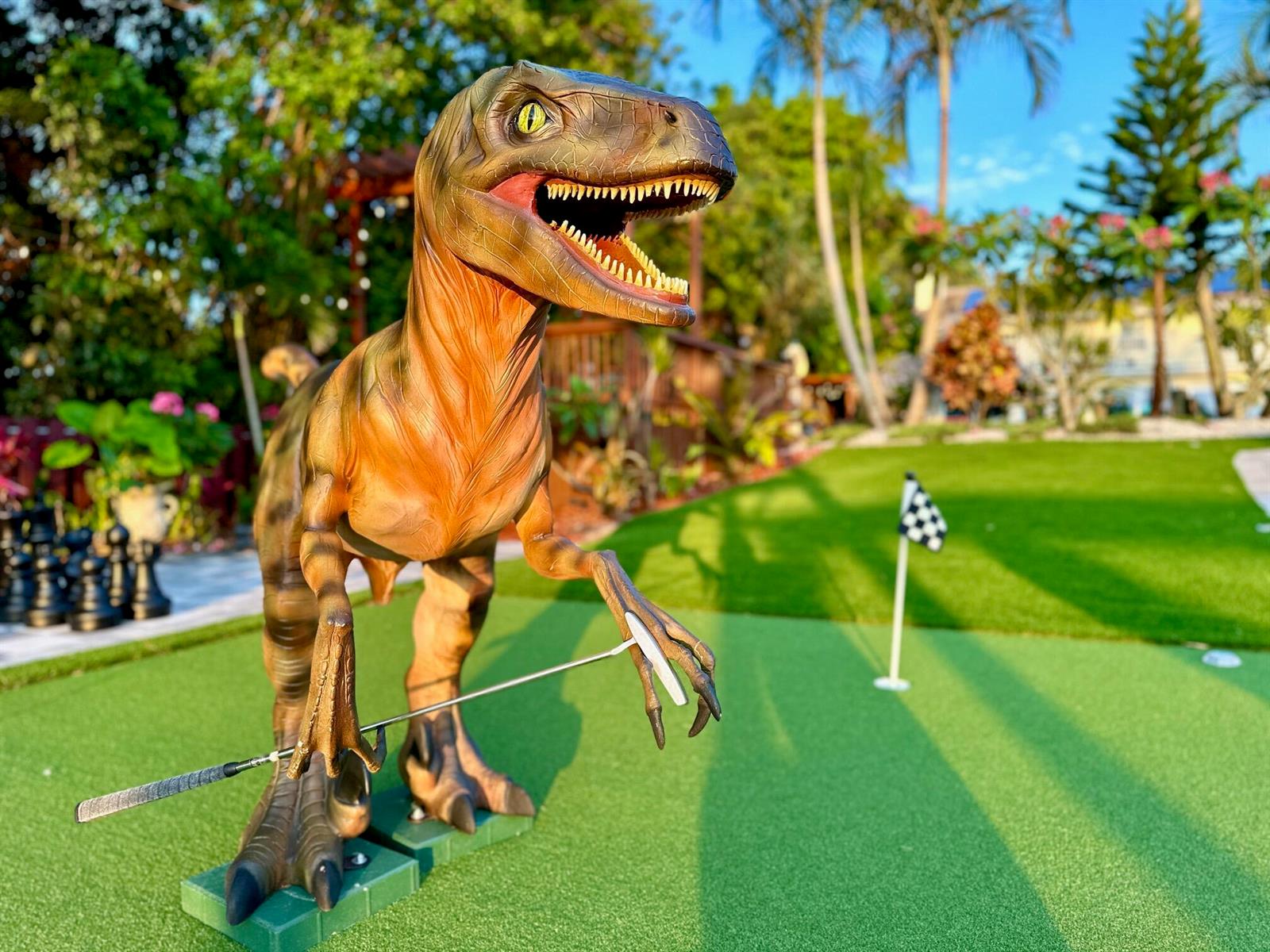 A dinosaur statue holding a golf club stands on a miniature golf course outdoors — 6850 Eastview Drive, Lake Worth FL 33462, LAKE WORTH, FL
