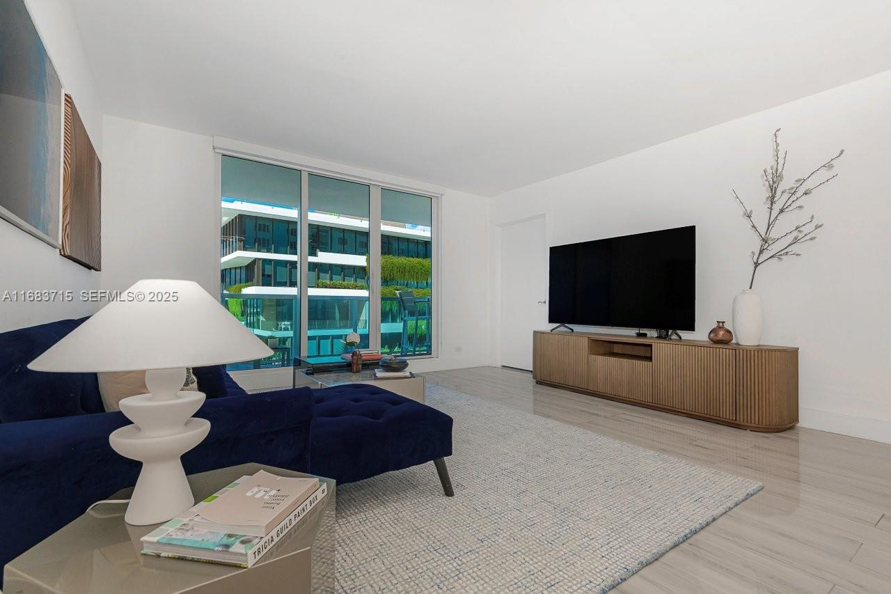 A living room features a blue sofa, a television on a wooden console, and floor-to-ceiling windows — 2301 Collins Ave # 534, Miami Beach FL 33139, MIAMI BEACH, FL