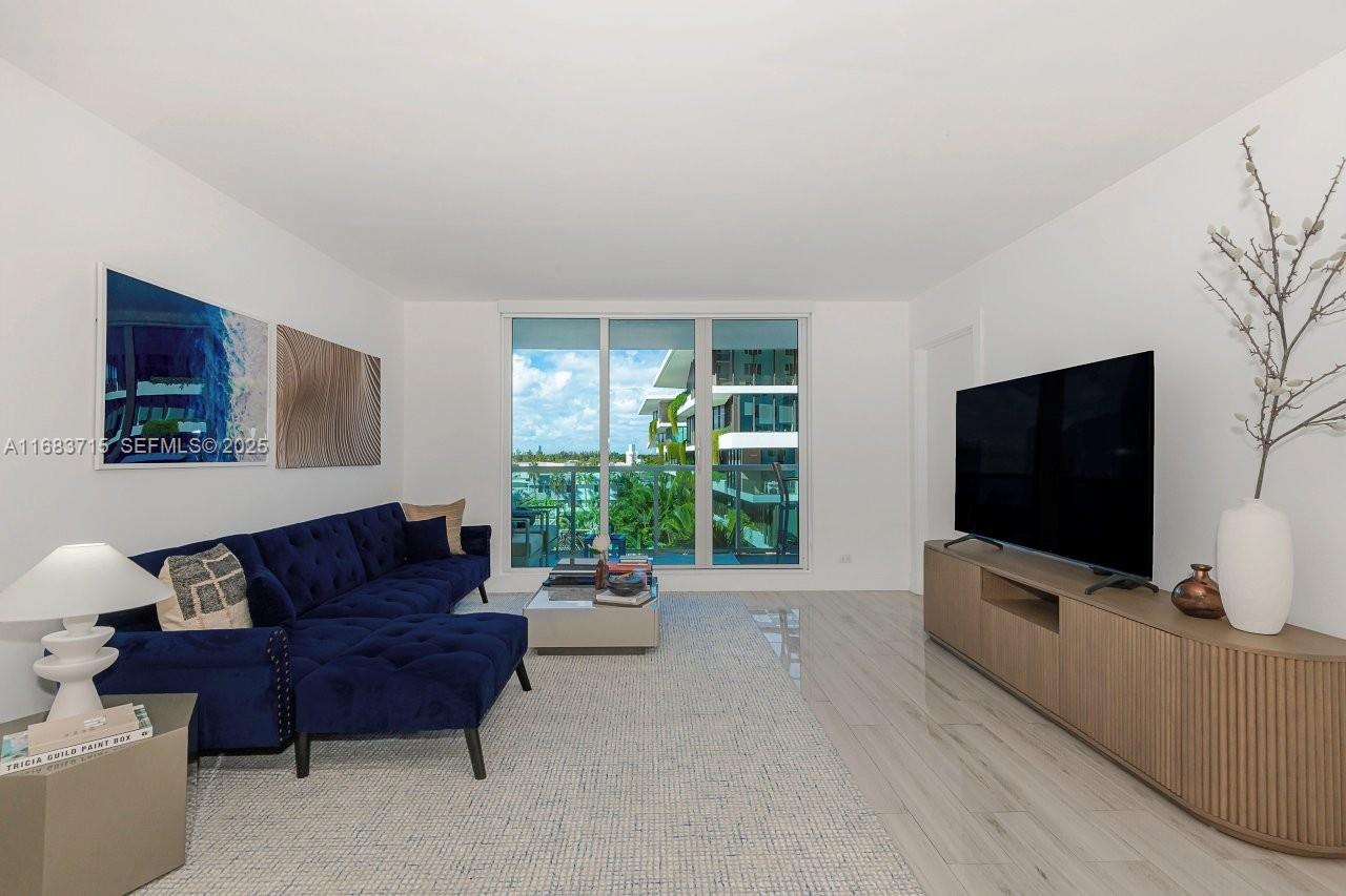 A living room features a blue tufted sectional, a large television, and floor-to-ceiling windows — 2301 Collins Ave # 534, Miami Beach FL 33139, MIAMI BEACH, FL