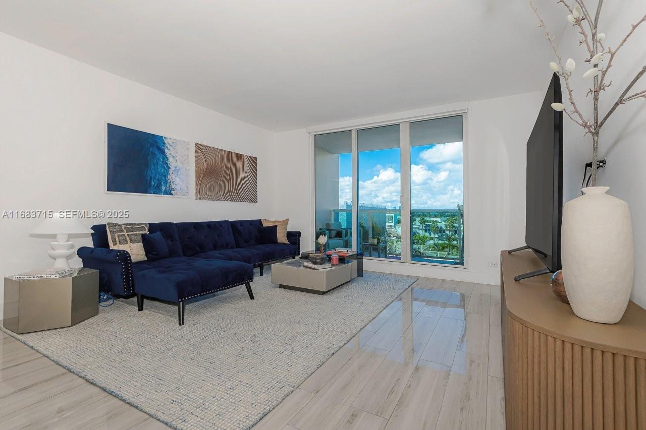 A living room features a blue sectional sofa, a coffee table, and floor-to-ceiling balcony windows — 2301 Collins Ave # 534, Miami Beach FL 33139, MIAMI BEACH, FL