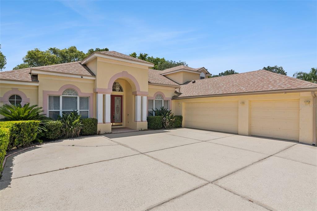 A single-story house with a large concrete driveway, arched entryway, and surrounding green landscaping — 126 SEVILLE CHASE DRIVE, WINTER SPRINGS, FL