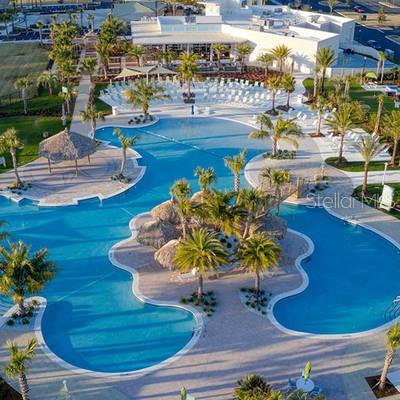 An aerial view of a large resort-style swimming pool with palm trees and lounge chairs — 1002 SEA SHELL COURT, DAYTONA BEACH, FL