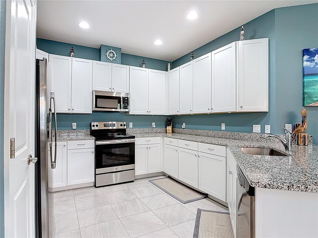 A kitchen features white cabinets, granite countertops, stainless steel appliances, and blue walls — 1002 SEA SHELL COURT, DAYTONA BEACH, FL
