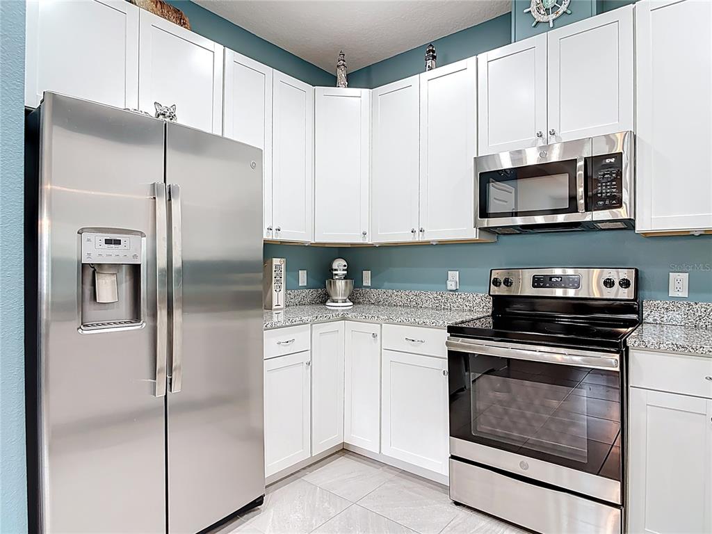 A kitchen features white cabinets, stainless steel appliances, and granite countertops against teal walls — 1002 SEA SHELL COURT, DAYTONA BEACH, FL