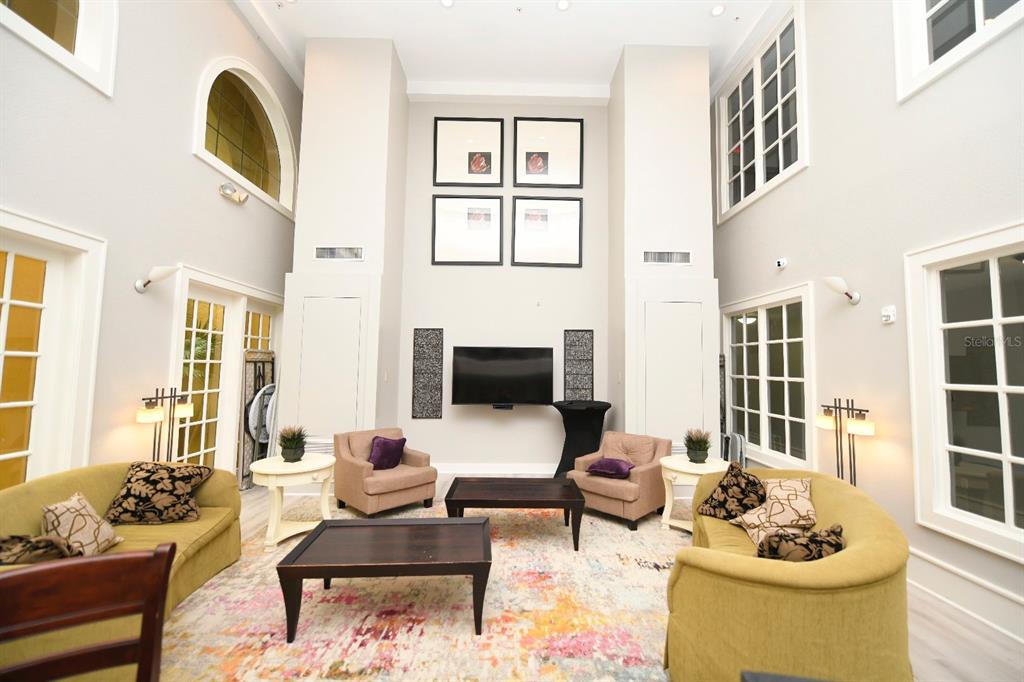A high-ceilinged living room features two curved sofas, two armchairs, and a wall-mounted television — 860 N ORANGE AVENUE UNIT 213, ORLANDO, FL