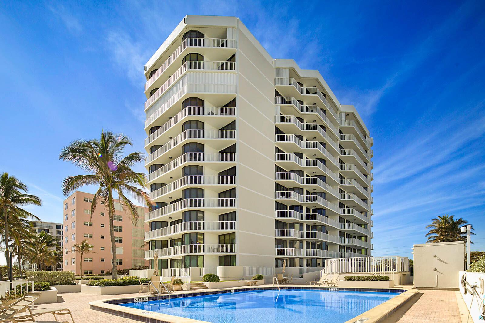 A tall white apartment building stands next to a swimming pool on a sunny day — 2917 S Ocean Boulevard # 405, Highland Beach FL 33487, HIGHLAND BEACH, FL