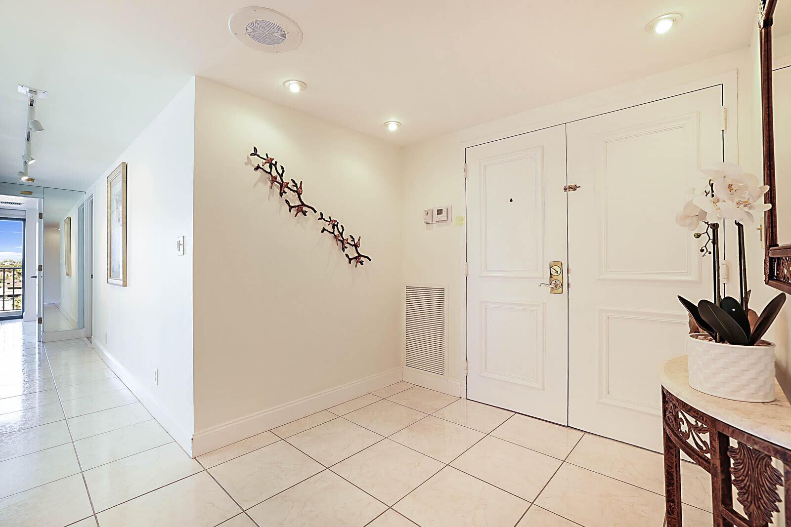 A bright entryway features white tile floors, double doors, and a decorative wall sculpture — 2917 S Ocean Boulevard # 405, Highland Beach FL 33487, HIGHLAND BEACH, FL