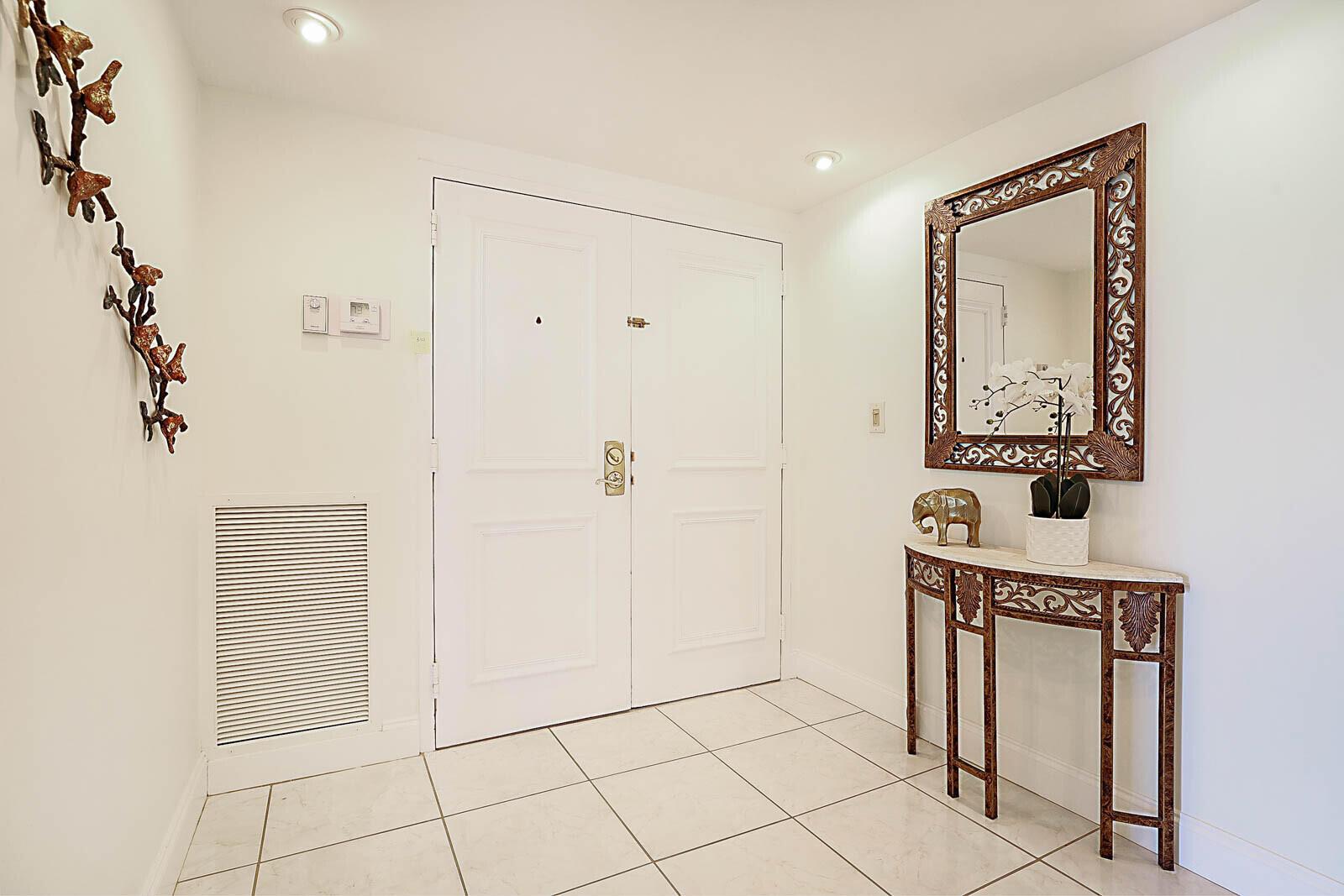 A white-tiled entryway features double doors, a decorative console table, and a wall-mounted mirror — 2917 S Ocean Boulevard # 405, Highland Beach FL 33487, HIGHLAND BEACH, FL