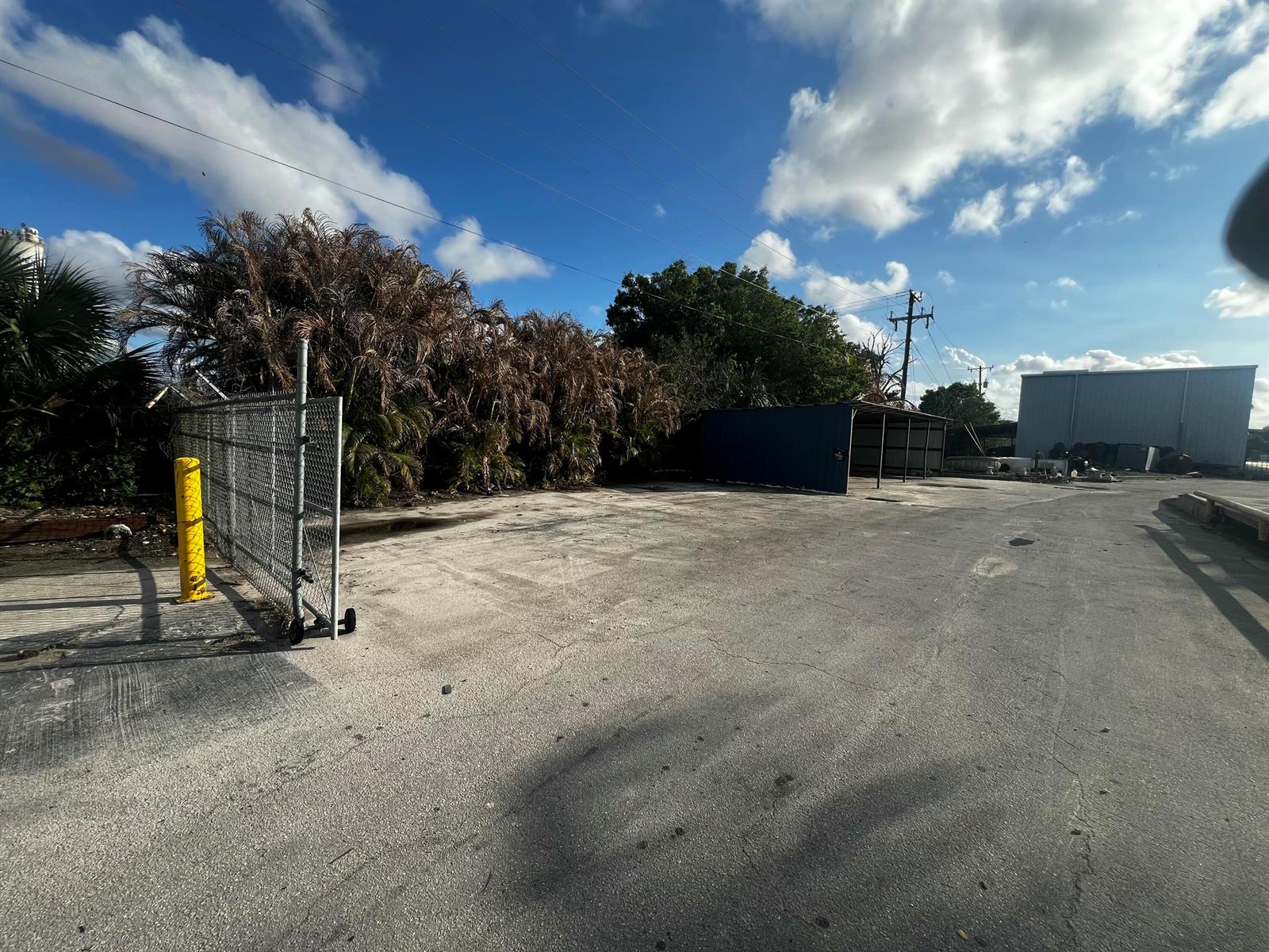 An outdoor paved lot features a chain-link gate, a small blue shed, and surrounding trees — 17250 SW Railroad Avenue, FL 34956, FL