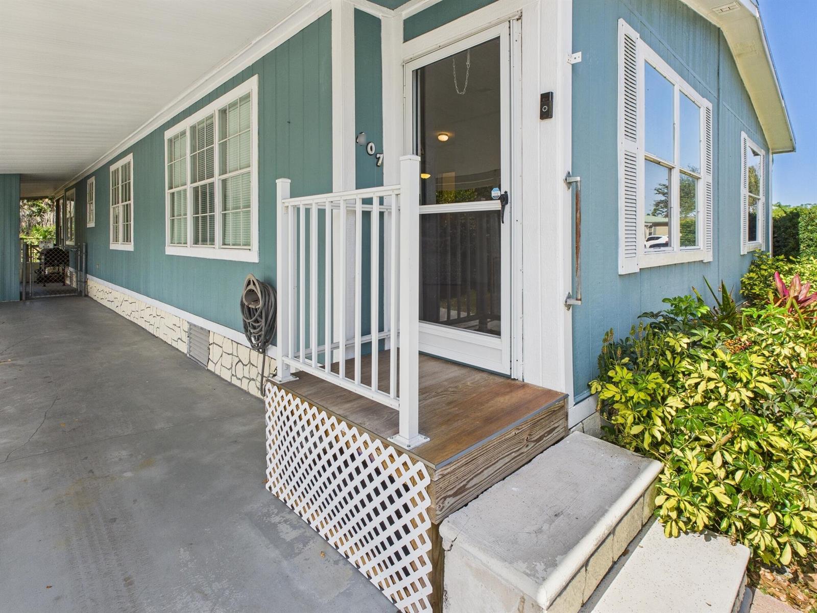 A blue mobile home exterior features a concrete carport, a small wooden porch, and landscaping — 407 NE 8th Avenue, Okeechobee FL 34972, OKEECHOBEE, FL