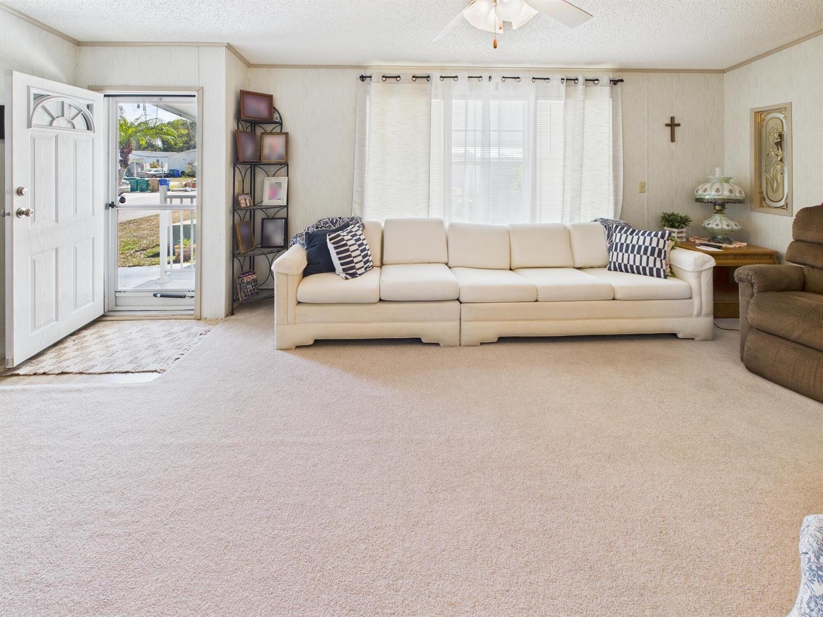 A living room features a white sofa, beige carpeting, and an open front door — 407 NE 8th Avenue, Okeechobee FL 34972, OKEECHOBEE, FL