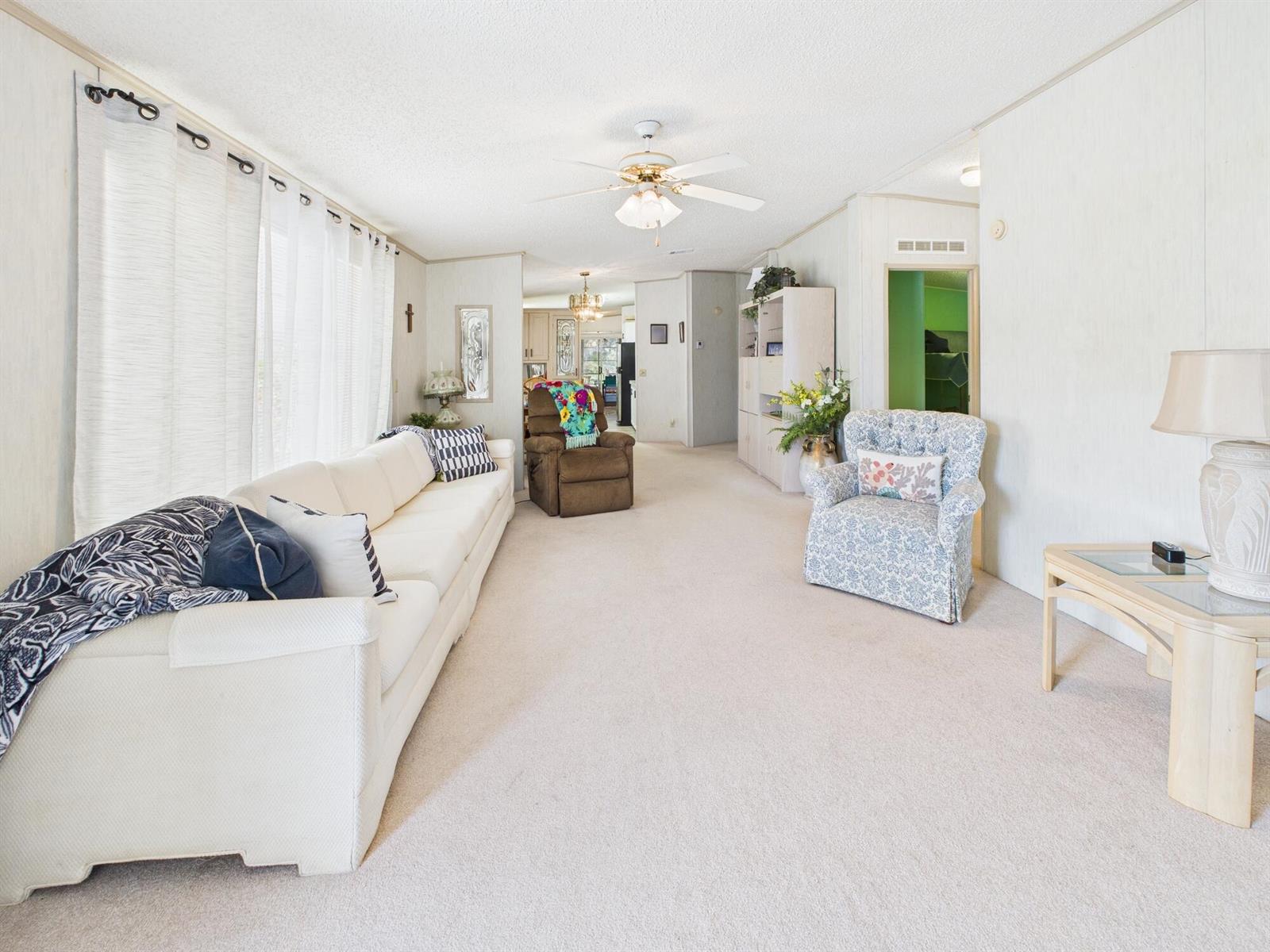 A living room features a white sofa, a floral armchair, beige carpeting, and a ceiling fan — 407 NE 8th Avenue, Okeechobee FL 34972, OKEECHOBEE, FL