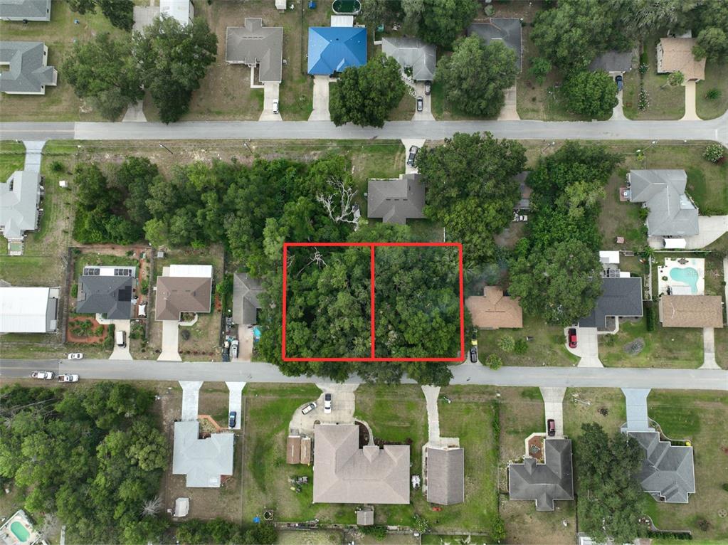 This aerial view shows two adjacent, tree-covered vacant lots outlined in red within a neighborhood — SE 157TH ST, SUMMERFIELD, FL