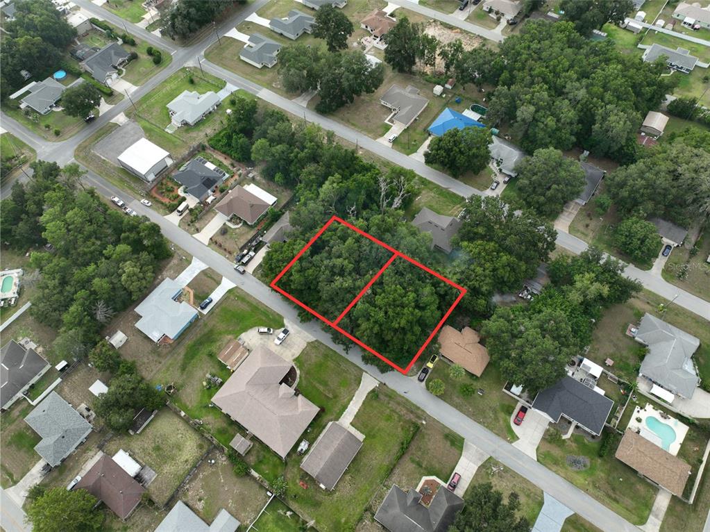 An aerial view shows two adjacent, wooded vacant lots outlined in red within a neighborhood — SE 157TH ST, SUMMERFIELD, FL