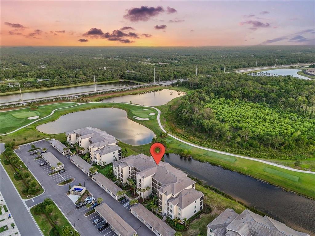 An aerial view shows a multi-story apartment building situated next to a golf course pond — 18028 GAWTHROP DRIVE UNIT 107, BRADENTON, FL