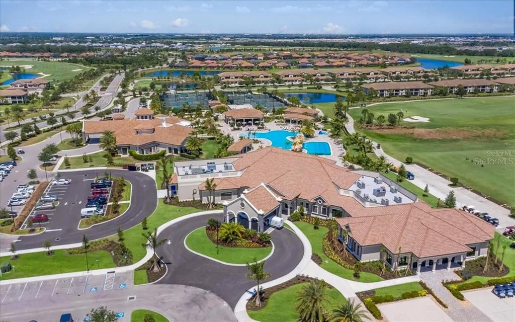 An aerial view of a community clubhouse with a swimming pool, tennis courts, and parking — 18028 GAWTHROP DRIVE UNIT 107, BRADENTON, FL