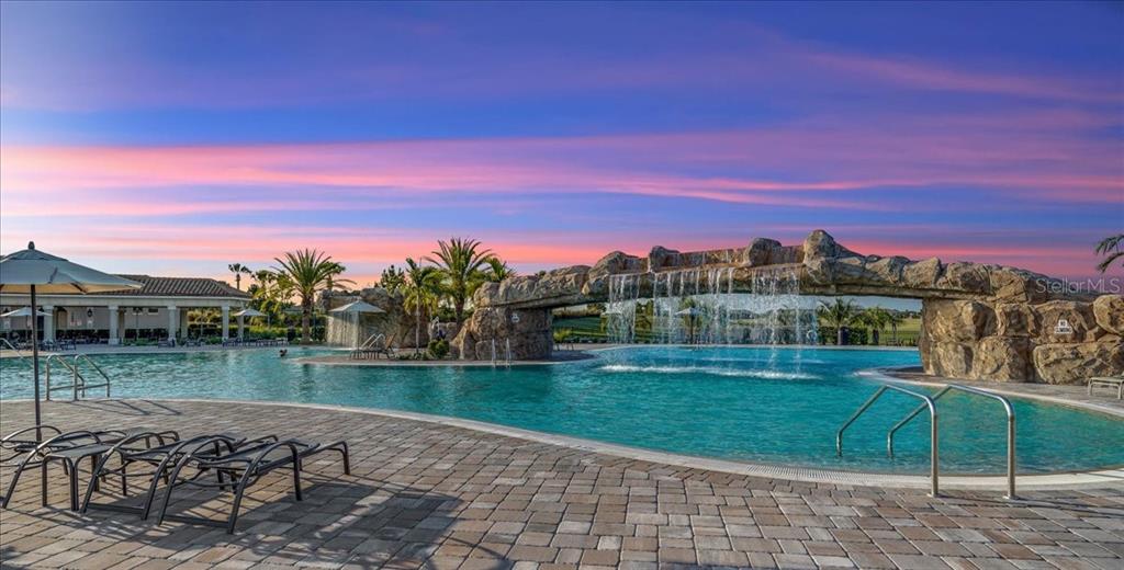 A resort-style swimming pool features a large rock waterfall feature and a paved deck area — 18028 GAWTHROP DRIVE UNIT 107, BRADENTON, FL