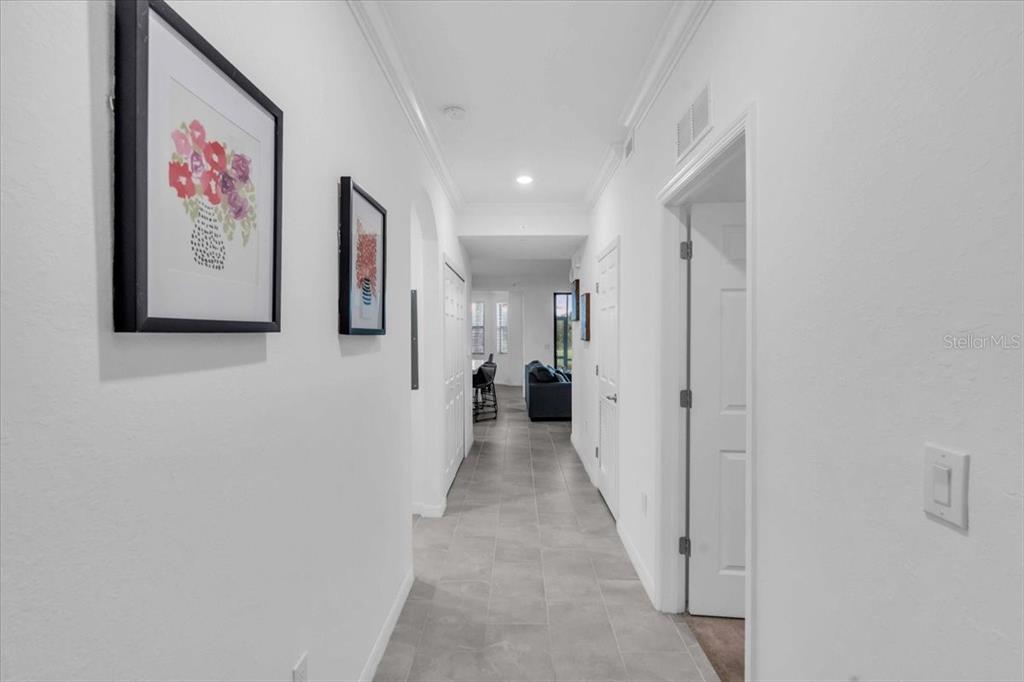 A bright hallway with white walls, gray tile flooring, and two framed pictures on display — 18028 GAWTHROP DRIVE UNIT 107, BRADENTON, FL