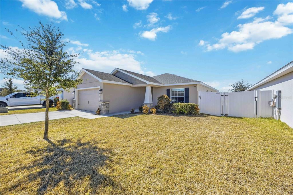 A single-story house with a tan exterior, a two-car garage, and a white vinyl fence — 1035 TROPEA LANE, AUBURNDALE, FL