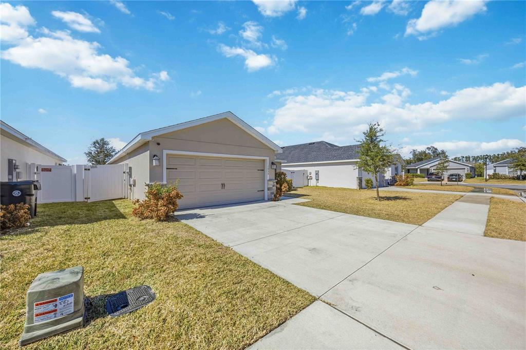 A beige single-story house features a two-car garage, a concrete driveway, and a grassy lawn — 1035 TROPEA LANE, AUBURNDALE, FL