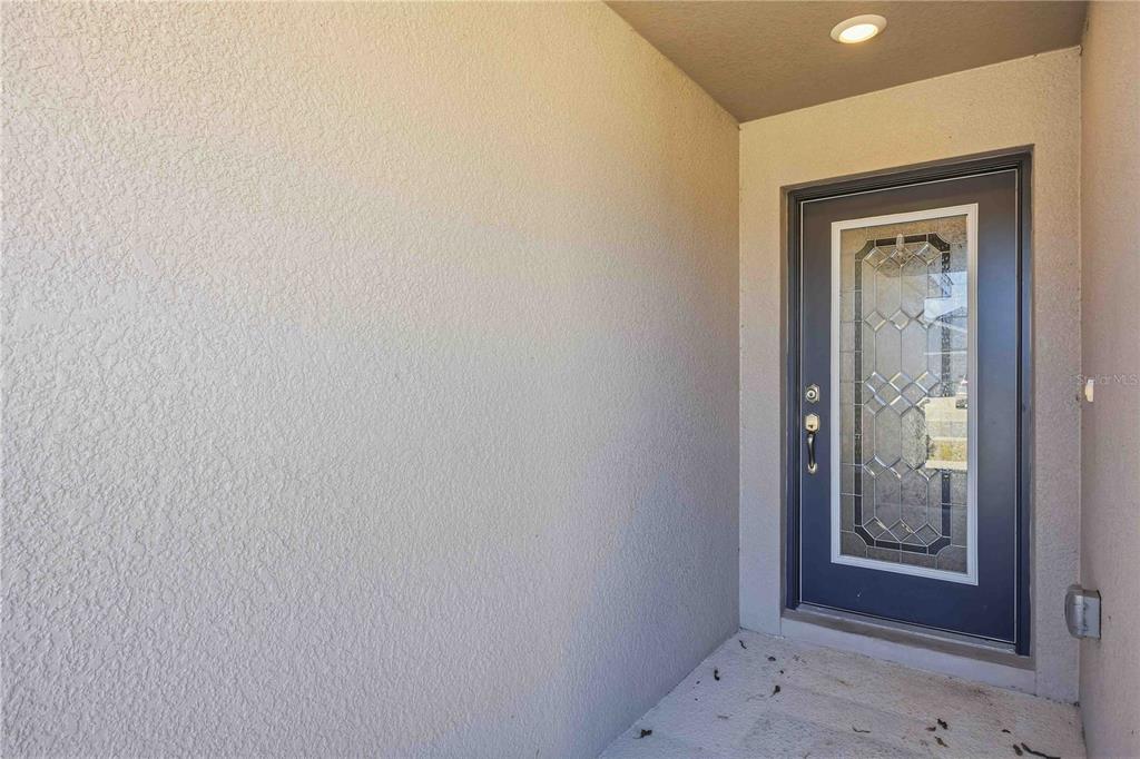 A covered entryway features a textured beige wall and a dark door with glass panels — 1035 TROPEA LANE, AUBURNDALE, FL