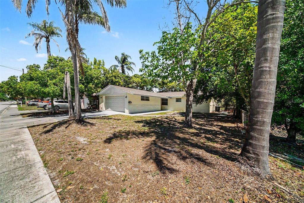 A single-story house with a light-colored exterior and a garage sits behind a palm-filled yard — 5301 82ND AVENUE N, PINELLAS PARK, FL