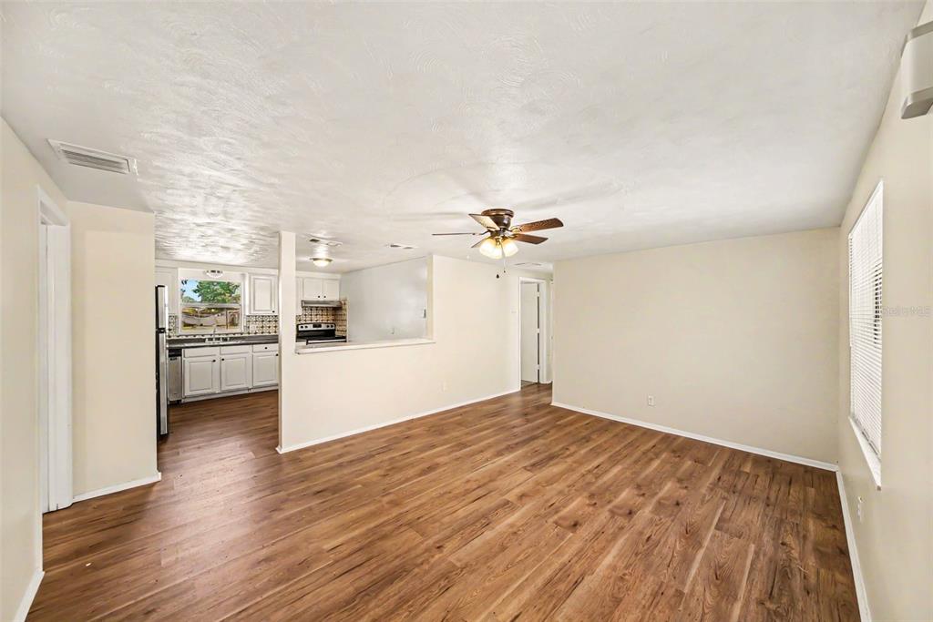 A living room with wood-look flooring and a ceiling fan opens to a white kitchen — 5301 82ND AVENUE N, PINELLAS PARK, FL