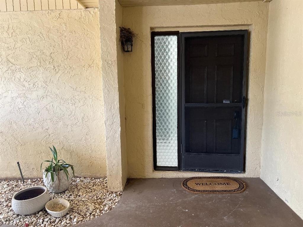 A front entryway features a dark screen door, a side window, and potted plants — 1220 13TH CIRCLE SE, LARGO, FL