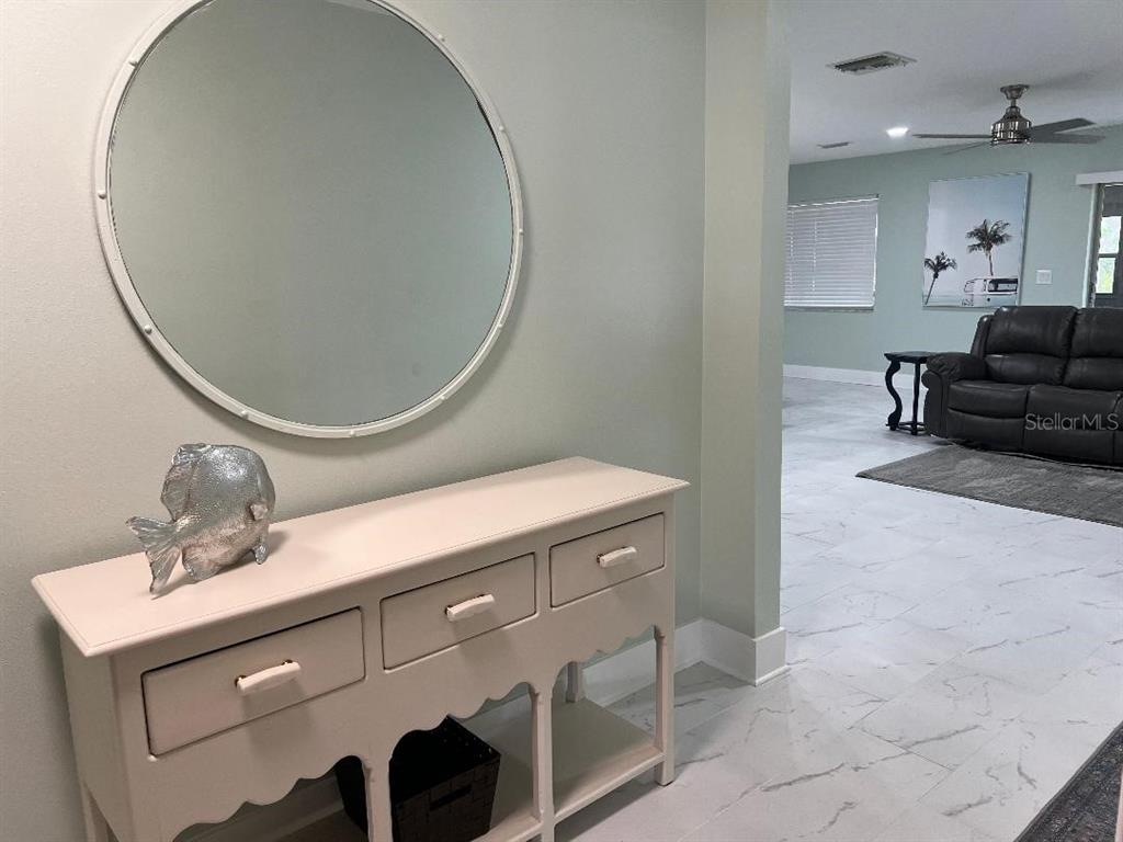 A light-colored console table with a round mirror sits in a foyer near a living room — 1220 13TH CIRCLE SE, LARGO, FL