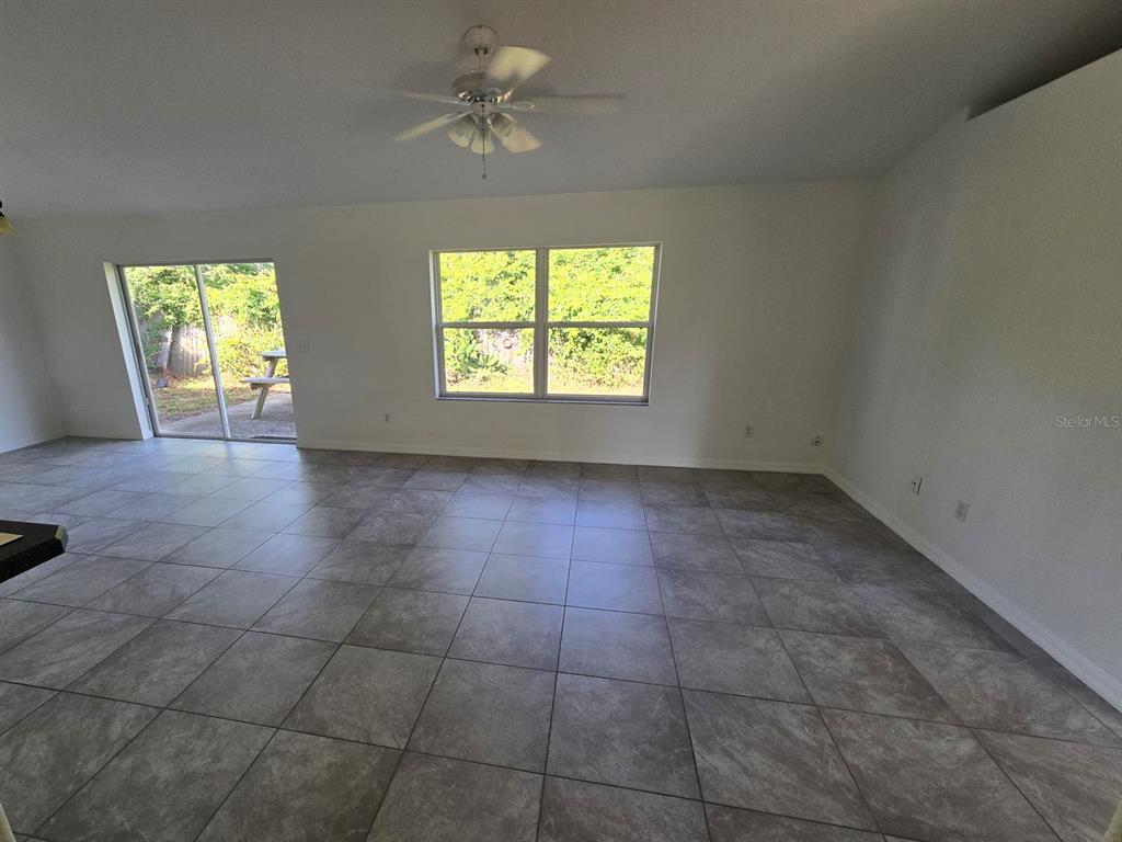 An empty living room features large gray floor tiles, white walls, and a ceiling fan — 2338 FERN PALM DRIVE, EDGEWATER, FL
