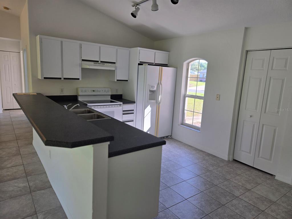 A kitchen features white cabinets, black countertops, a white refrigerator, and tile flooring — 2338 FERN PALM DRIVE, EDGEWATER, FL