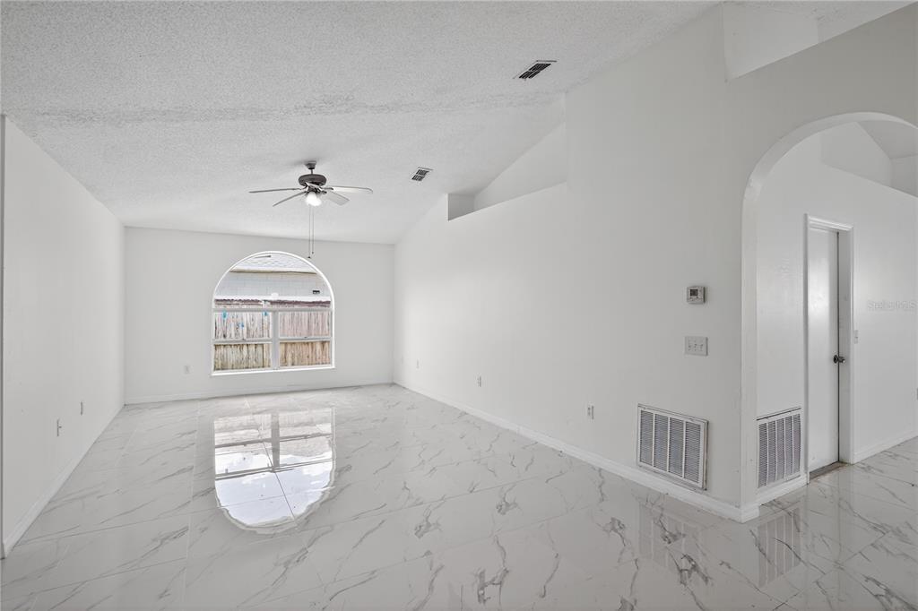A bright, open-concept kitchen and living area features white cabinetry and polished marble-look tile flooring — 1118 PERPIGNAN COURT, KISSIMMEE, FL
