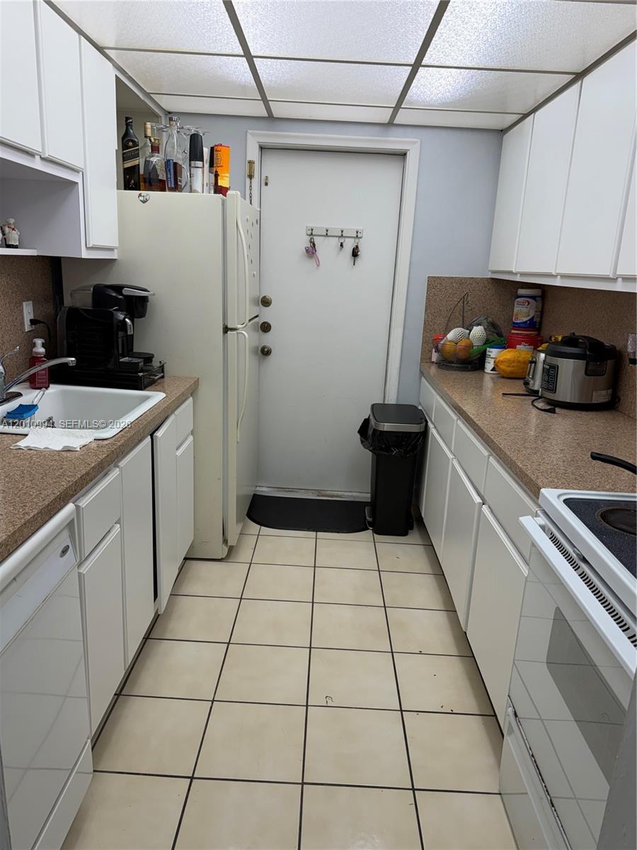 A galley-style kitchen features white cabinets, tan countertops, a white refrigerator, and tiled flooring — 7847 Miller Dr # A205, Miami FL 33155, MIAMI, FL
