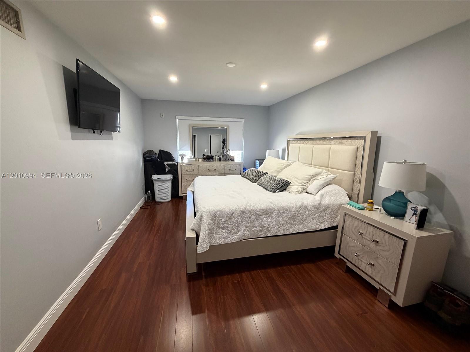 A bedroom features a bed with a tufted headboard, wood flooring, and a wall-mounted television — 7847 Miller Dr # A205, Miami FL 33155, MIAMI, FL