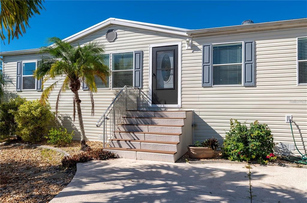 The exterior of a light-colored mobile home features a front staircase, a palm tree, and landscaping — 3101 BAMBOO COURT, PUNTA GORDA, FL