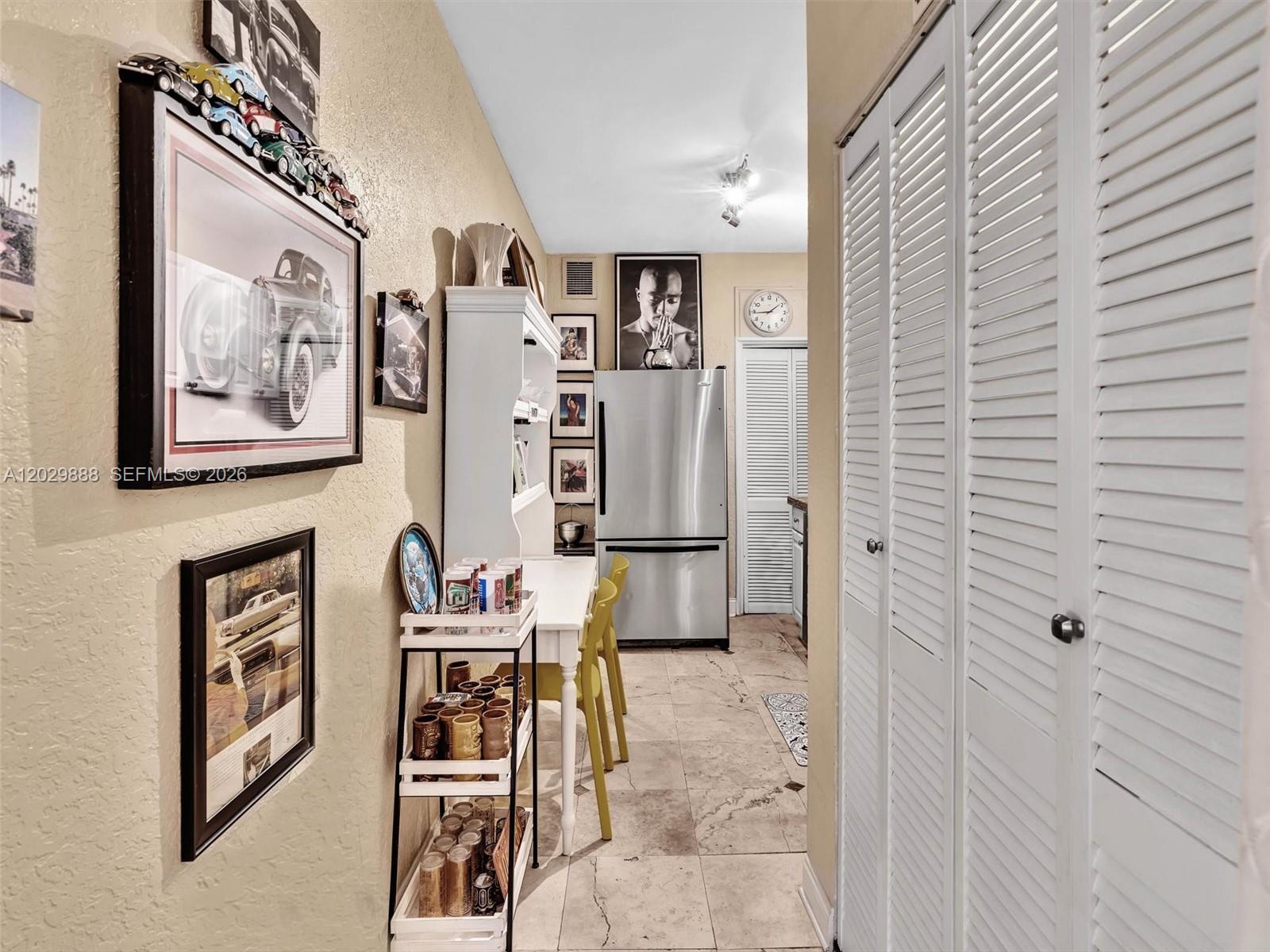 A narrow kitchen features a stainless steel refrigerator, white louvered doors, and a small dining area — 928 Euclid Ave # 2, Miami Beach FL 33139, MIAMI BEACH, FL