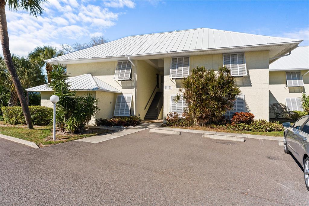 A two-story building with a metal roof, white stucco walls, and an outdoor staircase — 7310 SUNSHINE SKYWAY LANE S UNIT 112, ST PETERSBURG, FL