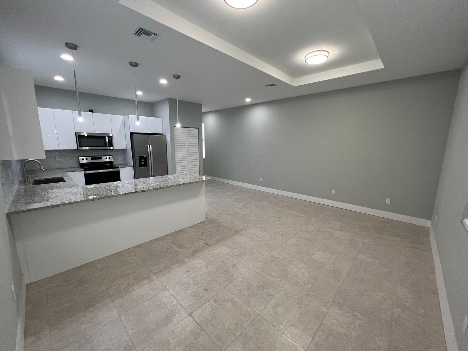 An open-concept kitchen with white cabinets, granite countertops, and tile flooring flows into a living area — 227 N E Street, FL 33460, FL