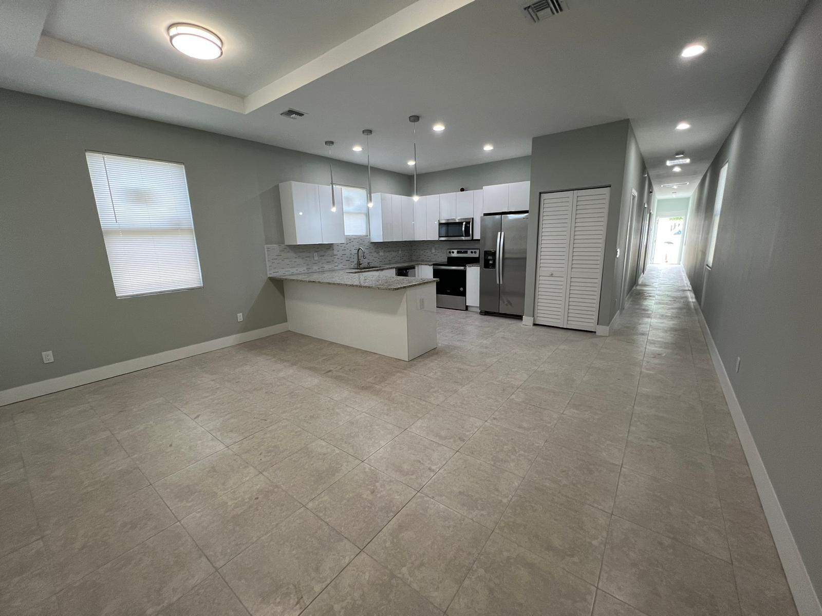 A modern kitchen with white cabinets, granite countertops, and stainless steel appliances opens to a hallway — 227 N E Street, FL 33460, FL