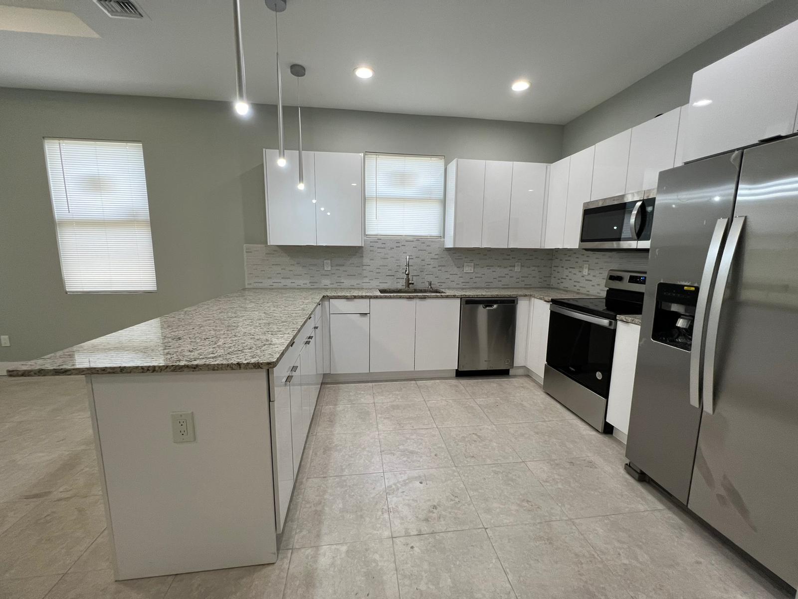 A kitchen features white cabinets, granite countertops, stainless steel appliances, and light tile flooring — 227 N E Street, FL 33460, FL