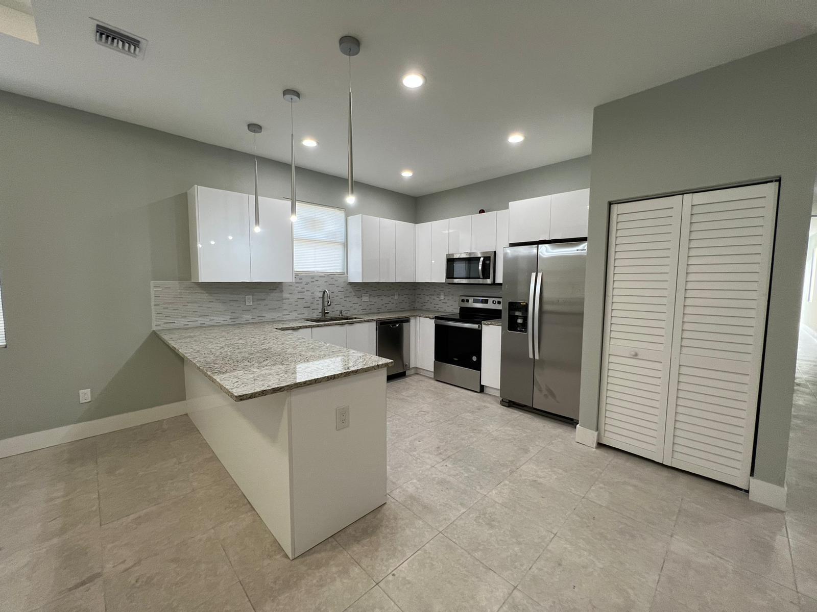 A modern kitchen features white flat-panel cabinets, granite countertops, stainless steel appliances, and tile flooring — 227 N E Street, FL 33460, FL